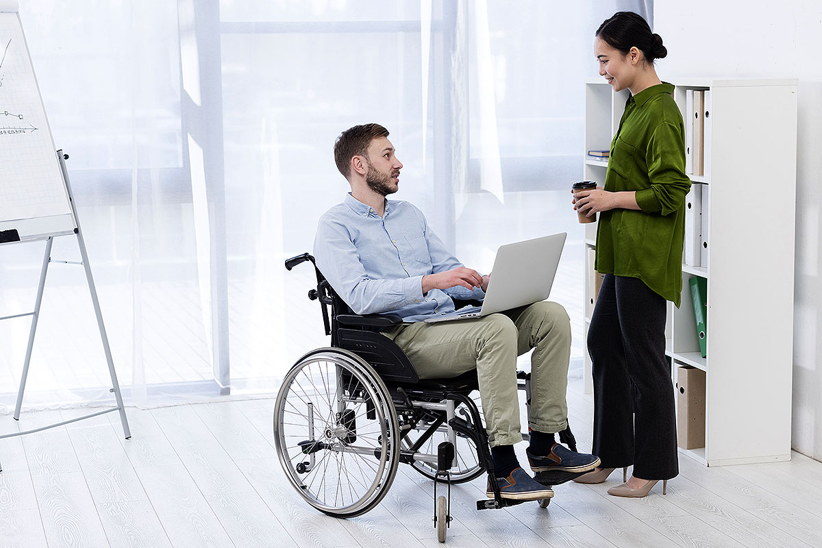 Un hombre en silla de ruedas charla con una compañera de trabajo en un entorno laboral